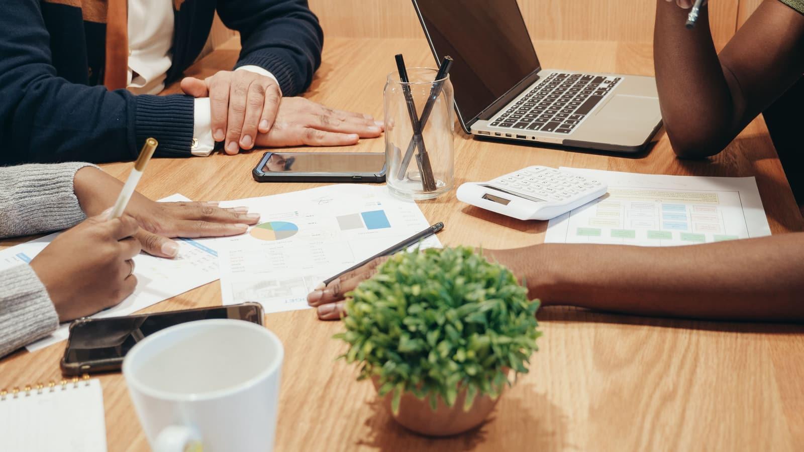 People reviewing printed charts and budget figures around a table with a laptop and calculator